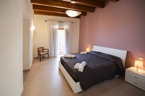 A bedroom with a large bed, a chair, a nightstand, and a window with curtains.