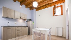 Een kleine keuken met houten kastjes, een witte tafel en transparante stoelen.