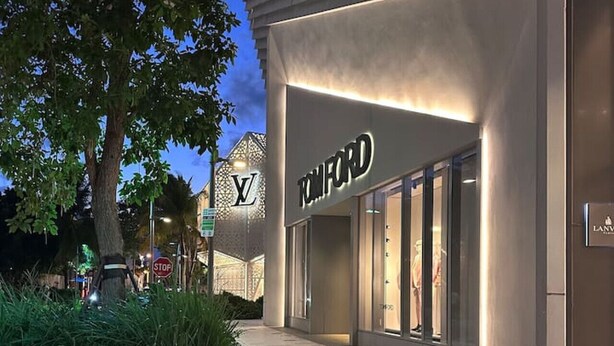 Une devanture de magasin avec une enseigne « Tom Ford », un panneau de signalisation indiquant un arrêt et un arbre en arrière-plan.