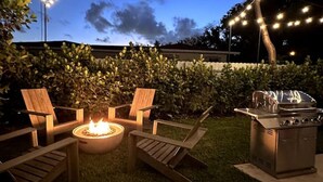 Une terrasse extérieure avec un foyer, des chaises en bois et un barbecue.