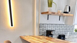 A modern kitchen with a wooden bar counter, two bar stools, a coffee machine, and a decorative plant. - Casa Memphis Updated Modern Home (El Paso)