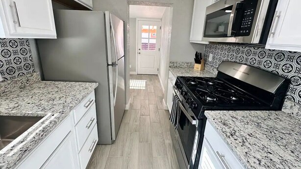 A kitchen with white cabinets, a stainless steel refrigerator, a microwave, a stove, and patterned backsplash tiles. - Casa Memphis Updated Modern Home (El Paso)