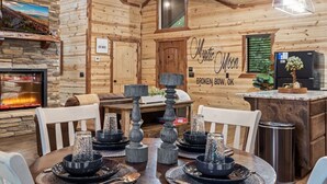 A wooden interior with a fireplace, a dining table set with dinnerware, and a kitchen area with a refrigerator.