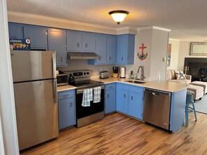 A modern kitchen with blue cabinets, stainless steel appliances, and a wooden floor.