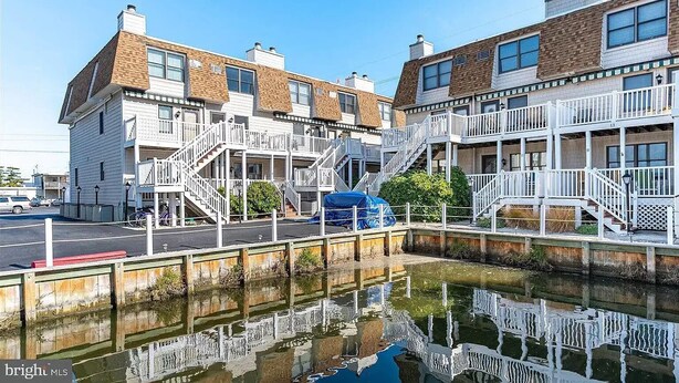 A waterfront property with multiple balconies, a covered walkway, and a canal in the foreground. - Fenwick Island, 1 block to beach, 2 BR condo, Sleeps 6, 2 parking spots (Fenwick Island)
