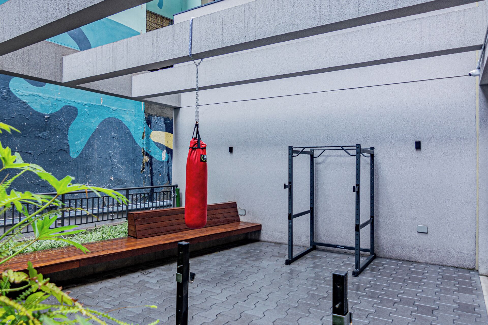 An outdoor gym area with a pull-up bar, a red punching bag, and a wooden bench.