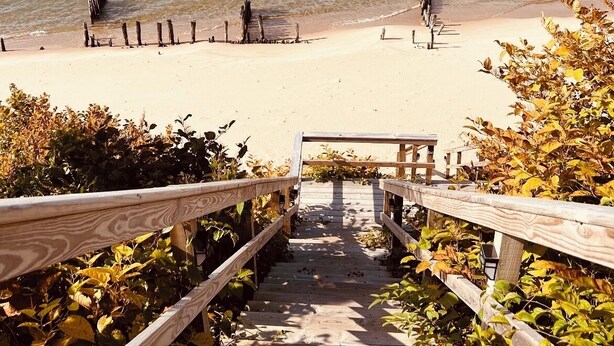 Un escalier en bois menant à une plage, avec une rambarde en bois et une vue sur l’océan.