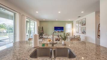 A kitchen with a granite countertop, double sink, and a dining area with a sofa and chairs.