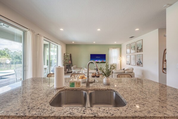 A kitchen with a granite countertop, double sink, and a dining area with a sofa and chairs. - Luxury 5BR Villa, Private Pool/Spa, 15 Min Disney! (Kissimmee)