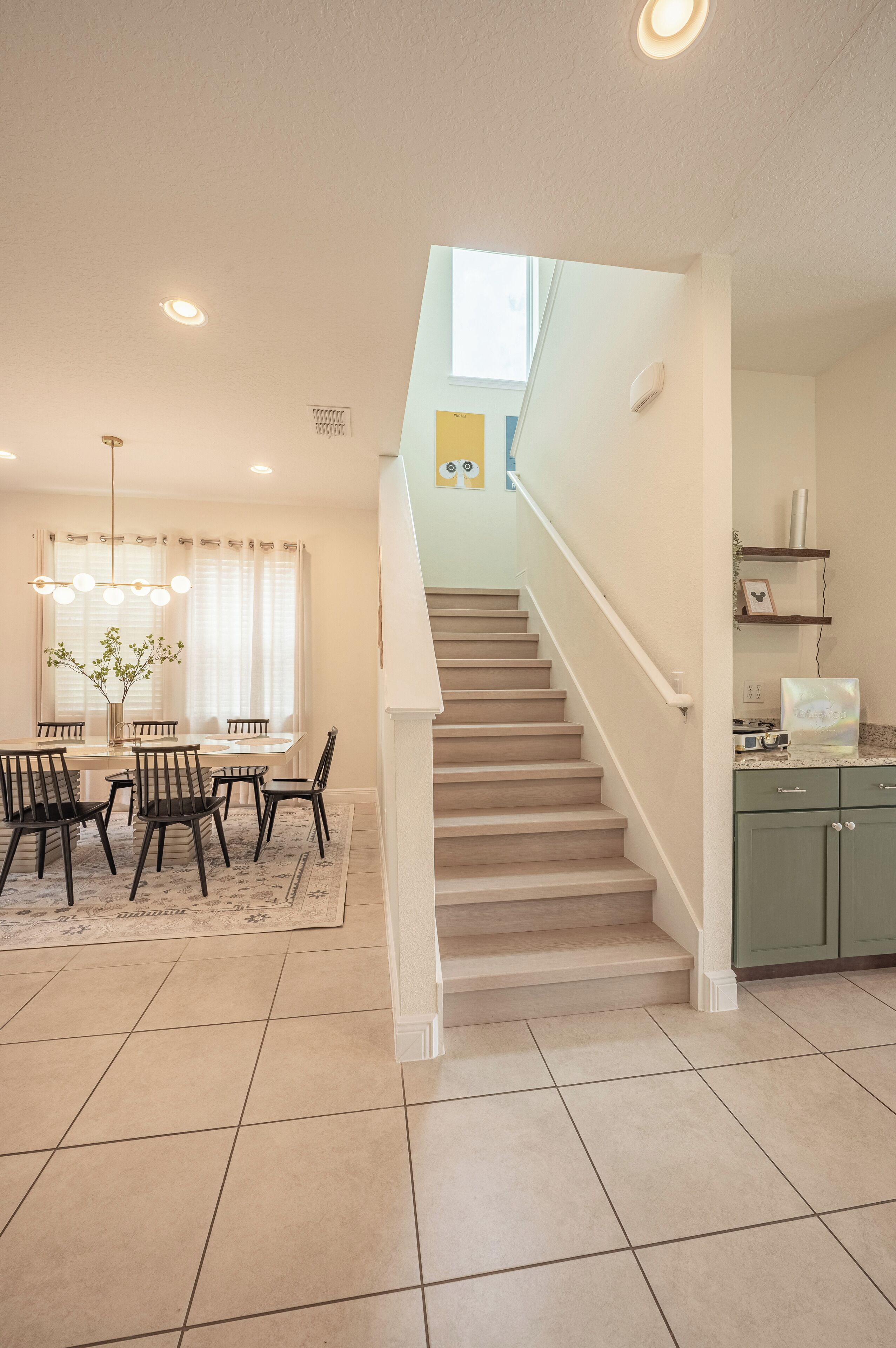 A modern kitchen with green cabinets, a dining area with a table and chairs, and a staircase leading to another level.