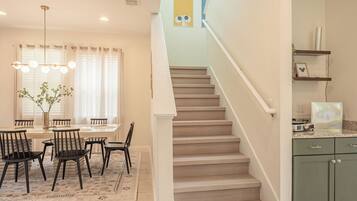 A modern kitchen with green cabinets, a dining area with a table and chairs, and a staircase leading to another level.