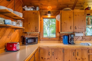 A wooden cabin kitchen with a toaster, microwave, coffee maker, and shelves with dishes and glasses. - Eagles Cove with kayaks, paddle boat, fire pit, pet friendly (Rangeley)
