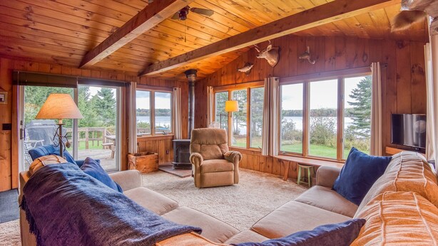 Interior acogedor de una cabaña con un sofá grande, una silla y una chimenea.