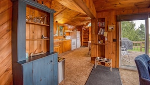 Interior de una cabaña de madera con cocina, comedor y vistas al exterior.