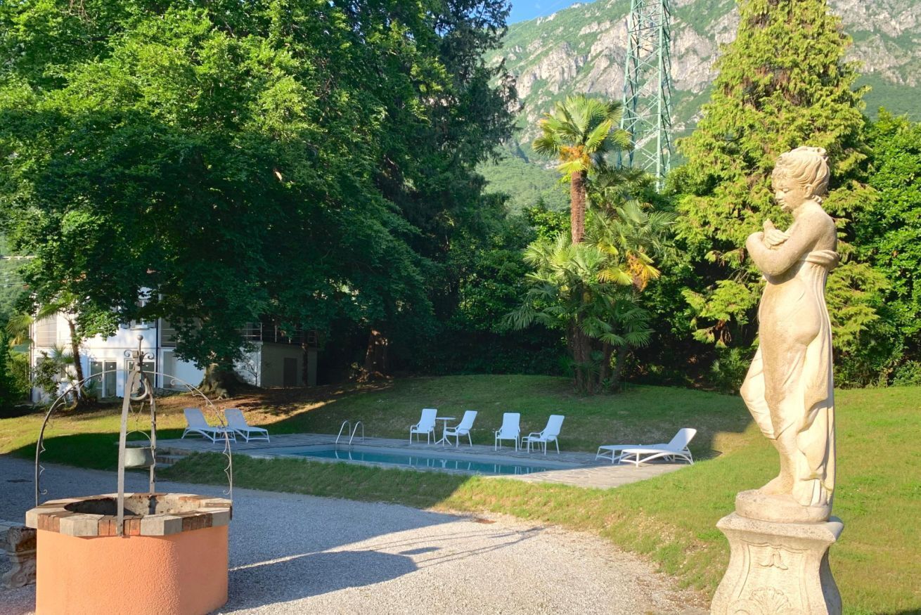A statue, a swimming pool, and lounge chairs in a garden setting.