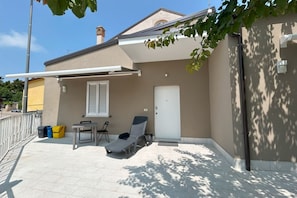 A covered outdoor area with a lounge chair, a table, and a door. - GuestHost - Modern 60 sqm apartment, ideal for 4 people, located on the ground floor of a renovated single house WITHOUT a lift (one step to access it). The accommodation is located in Pescara Colli, in a quiet residential neighborhood, where you can enj (Pescara)