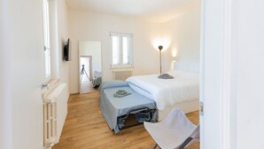 Un dormitorio con cama, una silla, un radiador y una ventana.