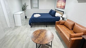 A modern bedroom with a bed, a sofa, a small table, and a dresser. - Casa Memphis Chic Basement Gem (El Paso)