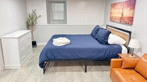 A modern bedroom with a bed, a dresser, a sofa, and a painting of the Eiffel Tower. - Casa Memphis Chic Basement Gem (El Paso)