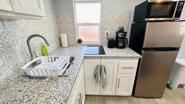 A modern kitchen with granite countertops, a stainless steel refrigerator, a microwave, and a coffee maker. - Casa Memphis Chic Basement Gem (El Paso)