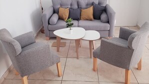 Ein Wohnzimmer mit grauem Sofa, zwei grauen Sesseln und einem kleinen weißen Tisch mit einer Pflanze.