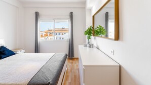 Een moderne slaapkamer met een bed, nachtkastje, dressoir, grote spiegel en raam met gordijnen.