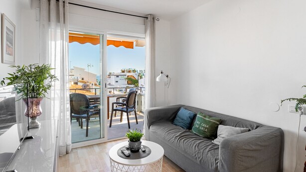 Een moderne woonkamer met een grijze bank, een klein rondend bijzettafeltje en een potplant.