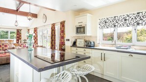A modern kitchen with a central island, white cabinetry, a microwave, and a toaster. There is a window with patterned curtains and a view of greenery outside. - 1 Homecroft Bungalows, Holiday Cottage Saundersfoot, Sleeps 6, 3 bedrooms,  bathrooms (Saundersfoot)