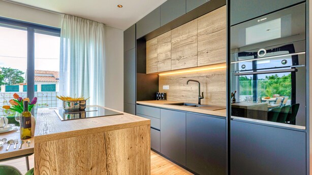 A modern kitchen with a wooden island, built-in appliances, and a view of the outdoors.