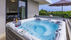A hot tub with a control panel, a bottle of champagne, and a glass of wine on a table.