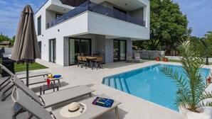 A modern two-story house with a swimming pool, outdoor furniture, and a patio area.