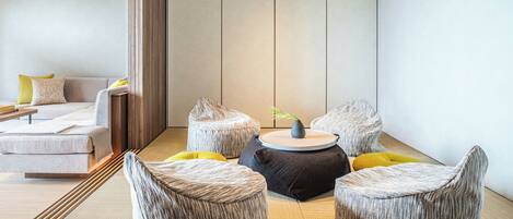 A modern hotel room with a sofa, two round ottomans, and a small table with a vase.