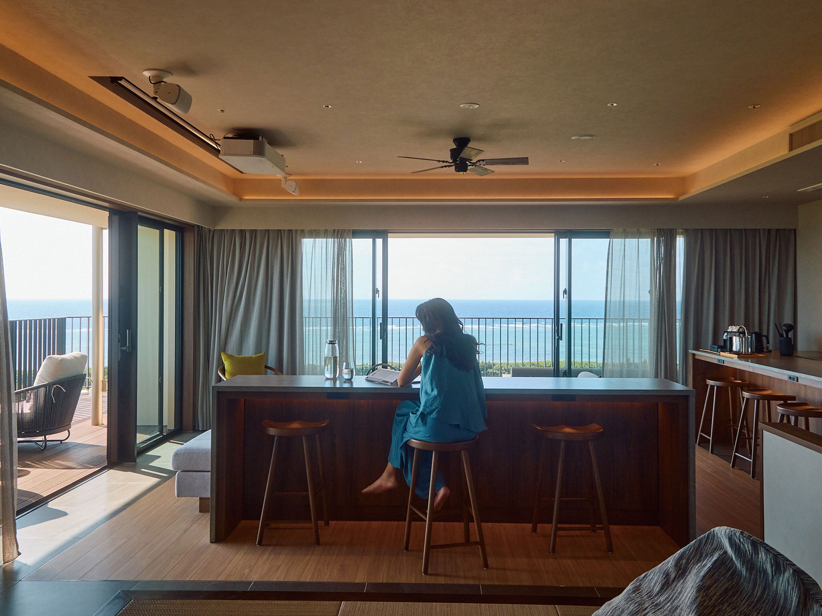 Een moderne keuken met een groot eiland, een eethoek met barstoelen en uitzicht op zee.