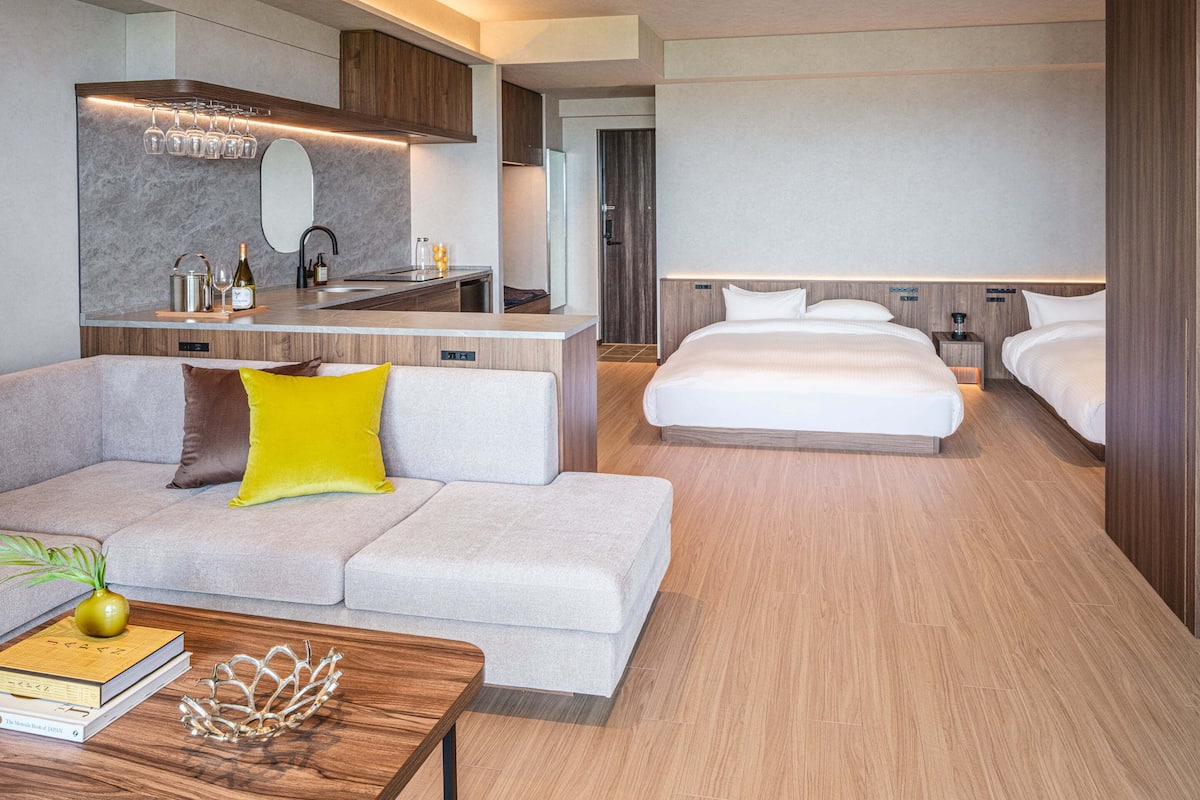 A modern hotel room with a sofa, a dining area, a kitchen, and a bed.