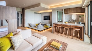 Un salon moderne avec un canapé, une table basse et un petit coin cuisine équipé de tabourets.