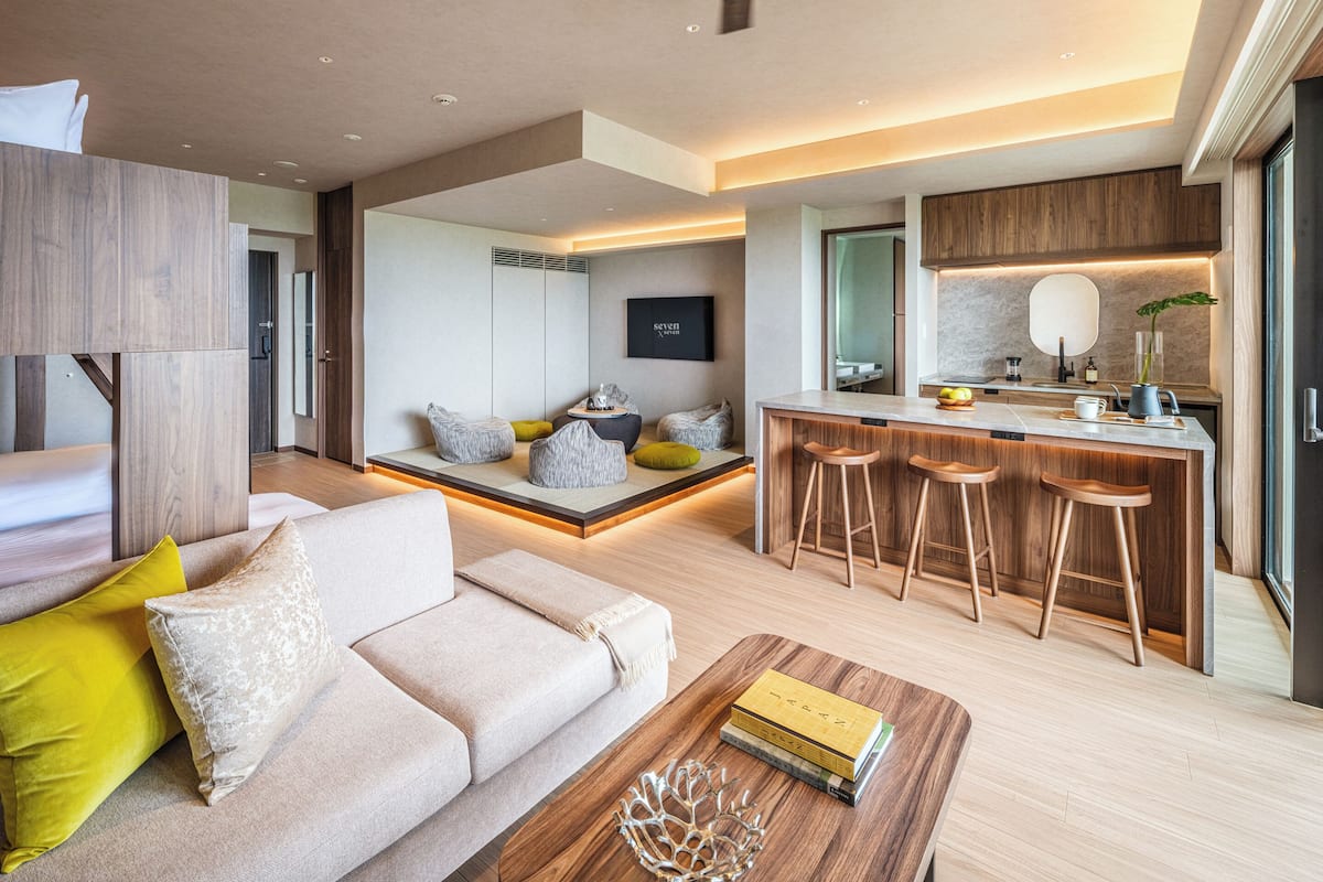 A modern living room with a sofa, coffee table, and a small kitchen area with stools.
