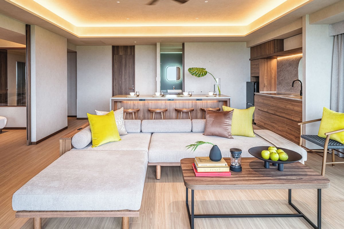 A modern living room with a sofa, coffee table, and a dining area with stools.