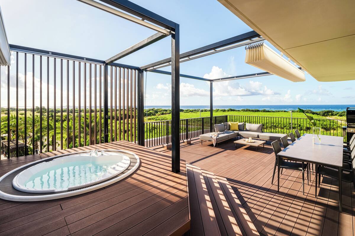 A wooden deck with a hot tub, outdoor seating, and a view of the ocean.