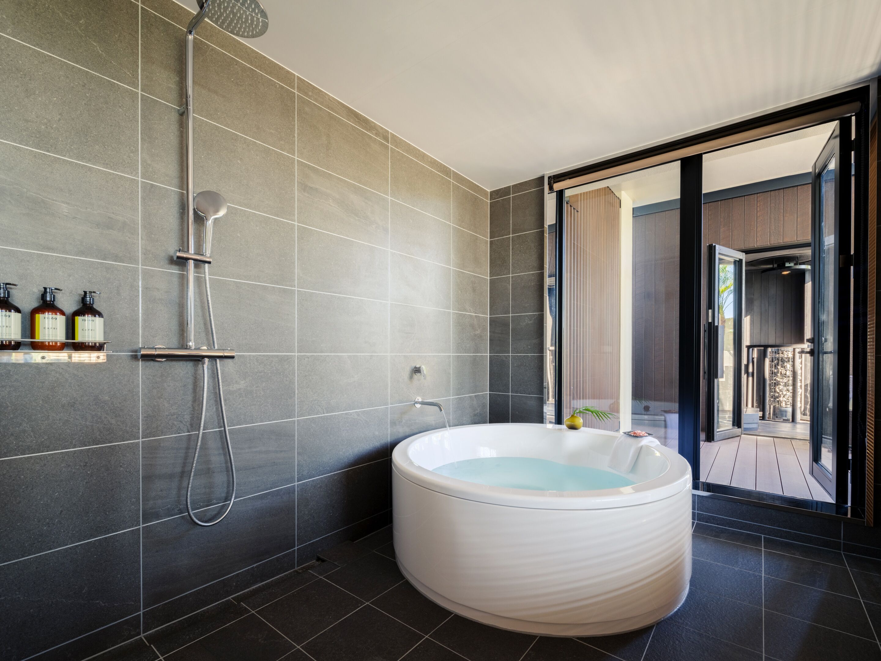 A modern bathroom with a large bathtub, a shower area, and a glass door leading to an outdoor area.
