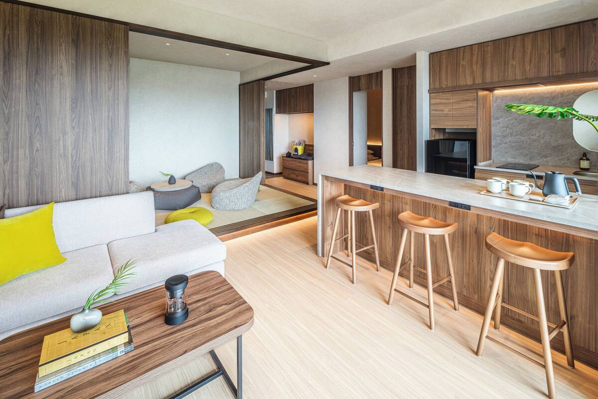A modern kitchen with wooden cabinets, a bar area with stools, and a seating area with a sofa and cushions.