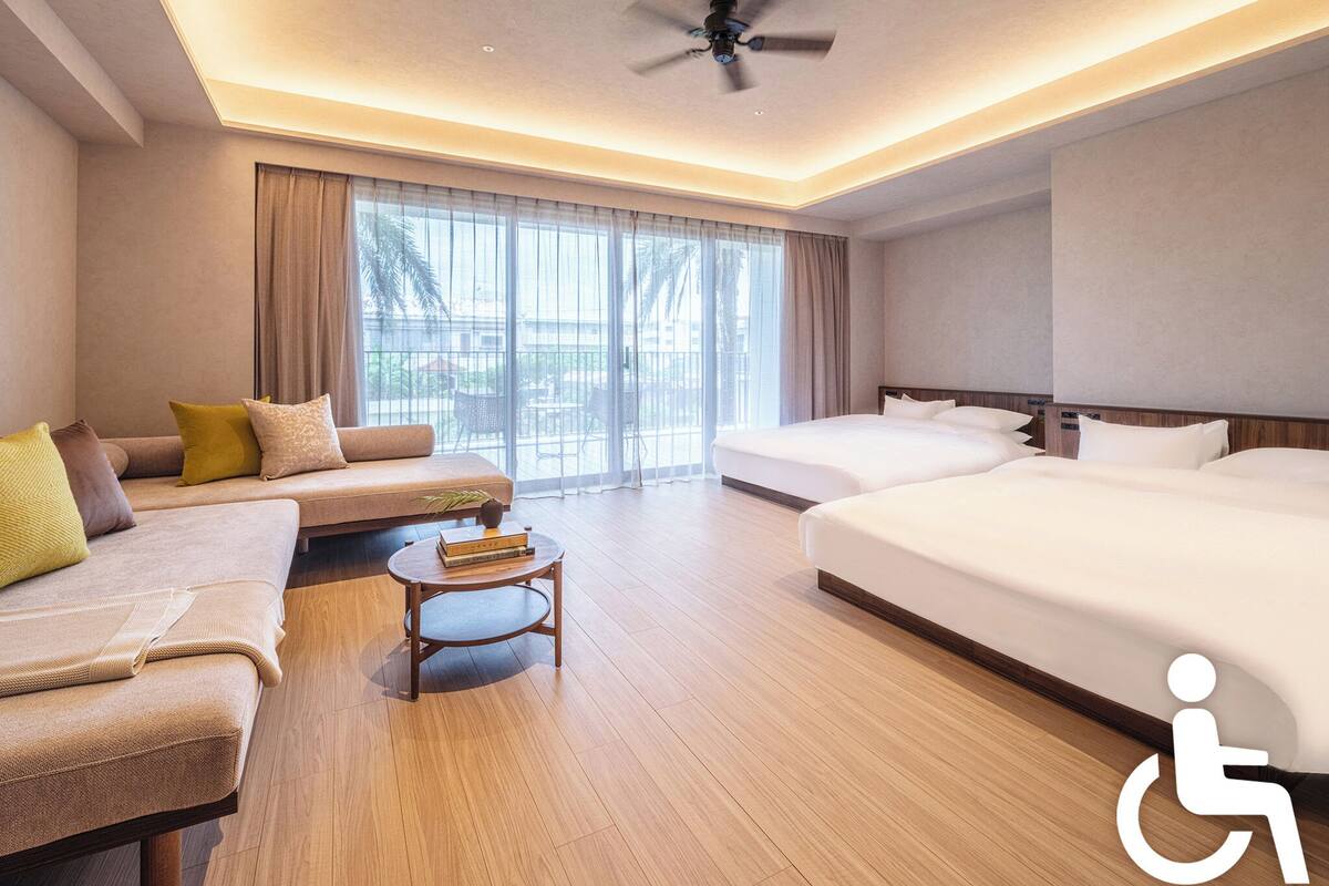 A hotel room with a sofa, two beds, a ceiling fan, and a view of the outdoors.