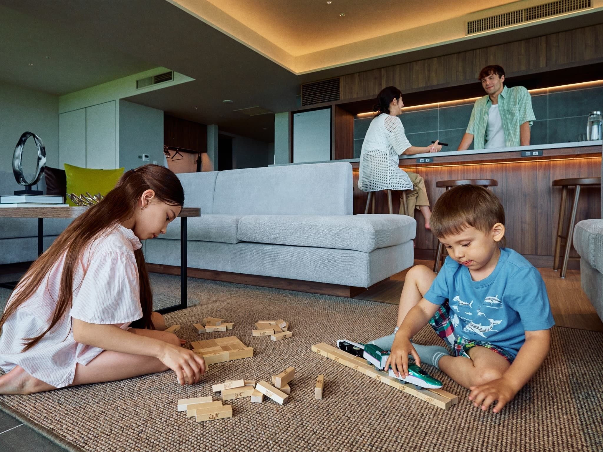 Una sala de estar moderna con un sofá gris, una mesa de centro y un niño jugando con bloques de madera.