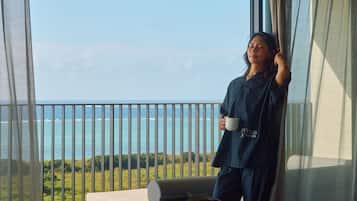 A balcony with a view of the ocean, a sofa, and a person holding a mug.