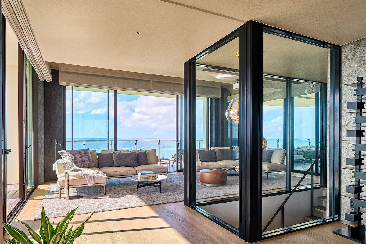 A spacious living room with a large sliding glass door leading to a balcony with a view of the sea.