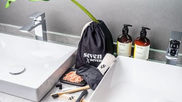 A bathroom with a white sink, a mirror, and toiletries including a black drawstring bag, two bottles of CAPRI body wash, and a green plant.