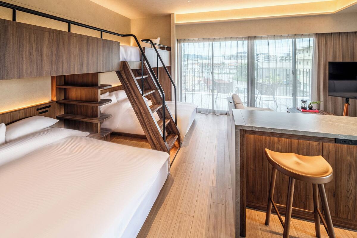 A modern hotel room with a bed, a desk with a chair, a TV, and a balcony with a view.