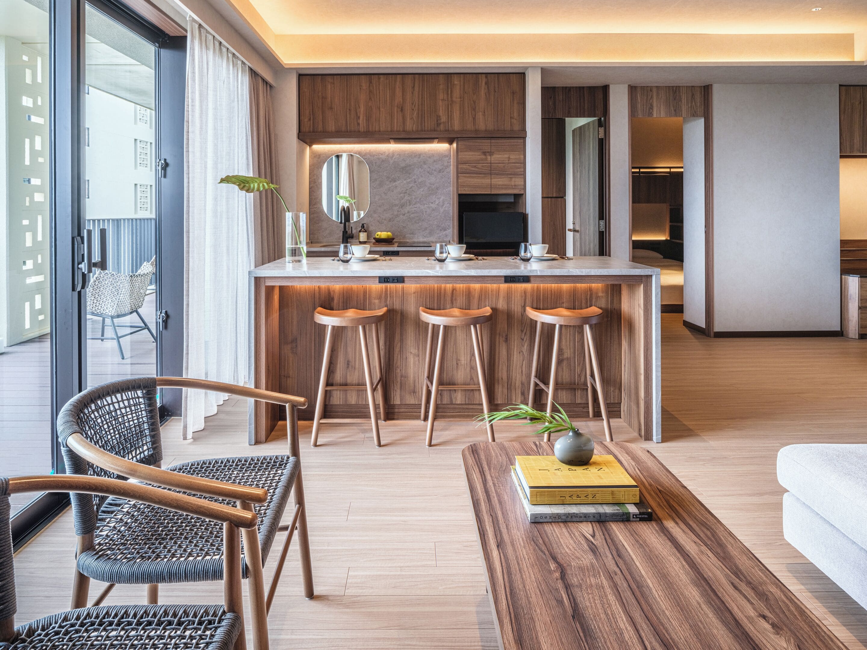 Una cucina moderna con isola centrale, sgabelli da bar in legno e zona pranzo con sedie in vimini.