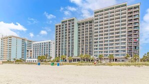 Um hotel à beira-mar com vários edifícios altos, varandas e uma praia de areia.