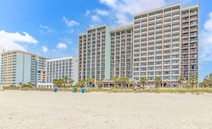 A beachfront hotel with multiple high-rise buildings, balconies, and a sandy beach.