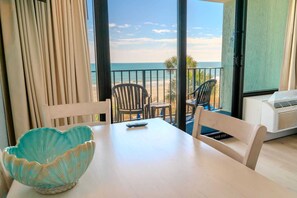 Ein Zimmer mit Tisch, Stühlen, einer Dekorationsschale und Blick auf den Strand.